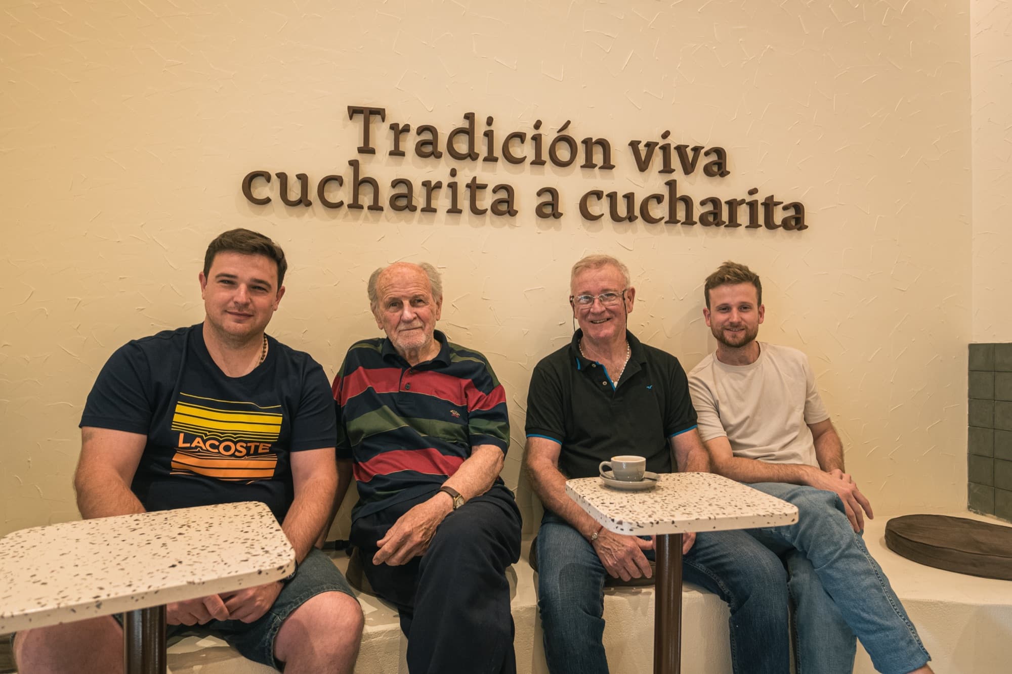 Cuatro integrantes de la familia Melano sentados bajo el cartel Tradición viva, cucharita a cucharita